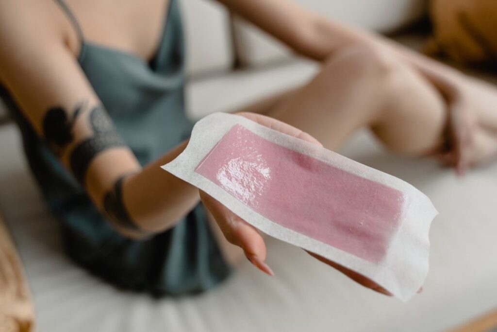 Close-up of a hand holding a pink cold-wax strip against a softly blurred indoor background